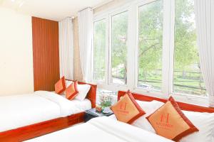 a hotel room with two beds and two windows at H Flower Hotel and Villa Đà Lạt in Da Lat