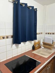 cocina con cortinas azules y fregadero en Appartement Rubis, en Cayenne