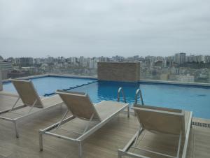 two chairs on a balcony with a large swimming pool at Hermoso condominio estilo Urban in Lima
