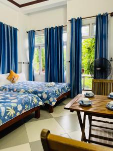 1 dormitorio con 2 camas, mesa y cortinas azules en Phuc Bao Center Local Homestay - 3 mins walk to Old Town en Hoi An