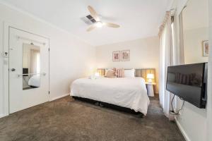 um quarto branco com uma cama e uma televisão de ecrã plano em Petal and Bloom - 3BR Family CBD em Bowden