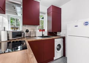 a kitchen with red cabinets and a white refrigerator at Radiant Serenity: 2BR Flat Sleeps 5 -Warm Ambiance in London