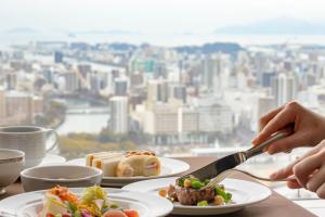 a table with plates of food with a view of a city at Rihga Royal Hotel Hiroshima in Hiroshima