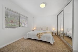 a white bedroom with a bed and a large window at Freelander Retreat in Katoomba