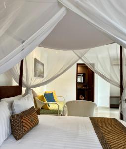 a bedroom with a white canopy bed with chairs at Villa Puriartha Ubud - CHSE Certified in Ubud