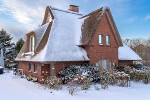 una casa con techo de paja en la nieve en Reetdach-Landhaus Mini Haubarg, en Tating