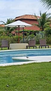 uma piscina com duas cadeiras e um guarda-sol em Apartamento condomínio Vila la Torre em Porto Seguro