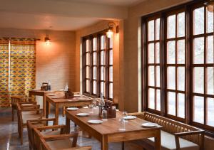 uma sala de jantar com mesas de madeira e janelas grandes em Moustache Koksar Luxuria em Khoksar