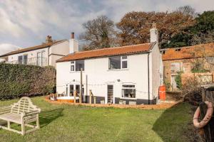 una casa blanca con un banco en el patio en Riverside Cottage - Norfolk Holiday Properties en Reedham