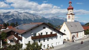 un bâtiment blanc avec une tour d'horloge avec des montagnes en arrière-plan dans l'établissement Gästehaus Elisabeth, à Tulfes