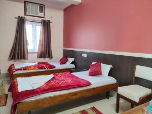 een slaapkamer met 2 bedden met rode muren en een stoel bij Hotel Vaishnavi near Baba Dham Temple in Deoghar
