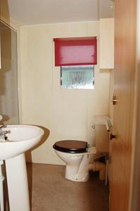 La salle de bains est pourvue de toilettes, d'un lavabo et d'une fenêtre rouge. dans l'établissement Caravan 309 Bryn Y Mor Beach Side Park, à Tywyn