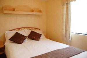 a bed with two pillows on it with a window at Caravan 309 Bryn Y Mor Beach Side Park in Tywyn