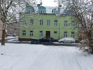 une rue enneigée en face d'un bâtiment vert dans l'établissement Apartment 35m2, à Karlovy Vary
