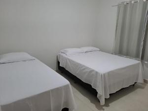 duas camas com lençóis brancos num quarto em Casa de praia em Mucuri Bahia em Mucuri