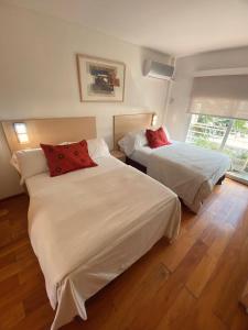 a bedroom with two beds with white sheets and red pillows at Apart Hotel Rio Grande in Rosario