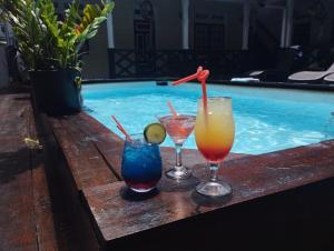 3 bebidas en una mesa junto a la piscina en Zeelandia Suites, en Paramaribo