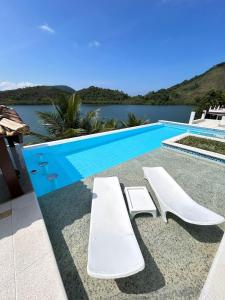 a swimming pool with two white lounge chairs next to it at Oásis Beach House in Angra dos Reis