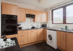 cocina con armarios de madera, lavadora y secadora en Logie Green Road Apartment, en Edimburgo