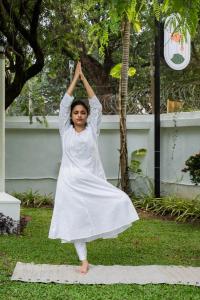 The Sacred Lotus Ayurveda Wellness Retreat في كوتشي: امرأة ترتدي ثوب أبيض تقوم بوضع اليوغا