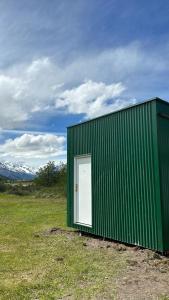 ein grünes Gebäude mit einer weißen Tür auf einem Feld in der Unterkunft Fitz Roy Hostería de Montaña - El Chaltén in El Chalten