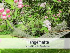eine Hängematte vor einem Baum mit rosa Blumen in der Unterkunft Bio Ferienhof Wichtelweide - Fewo Thymian in Fehmarn