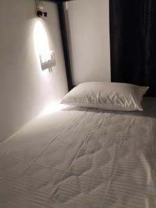 a white bed with a pillow and a light on the wall at The Chill House in Cochin