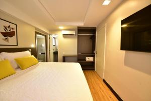 a bedroom with a white bed and a flat screen tv at Golden Tulip Goiania Address in Goiânia