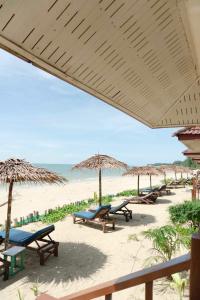 una playa con mesas y sombrillas de paja y el océano en Pranee Beach Bungalows en Ko Kho Khao