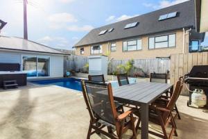 a patio with a wooden table and chairs and a house at Opal of Orewa with pool, spa and ocean views in Orewa