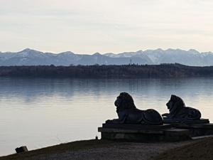 a statue of two lions sitting next to a body of water at Central Starnberg and surrounded by nature in Starnberg +13 photos