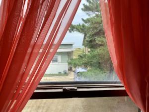 a window with red curtains looking out at a house at Break Side Studio #5 apts in North Camellia Acres +14 photos