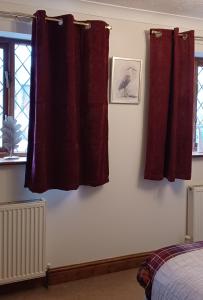 a bedroom with two red curtains and a bird on the wall at Woodpeckers Cottage B&B in Pett