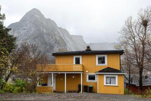 uma casa amarela com uma montanha ao fundo em Cozy House By The Fjord In The Heart Of Lofoten em Reine
