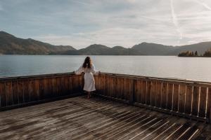 a woman in a white dress standing on a boardwalk by a lake at Wallerei Walchensee in Walchensee