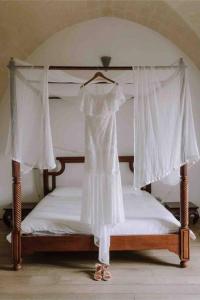Villa CastelliにあるMasseria Angiulli Piccolo Contrada Angiulli 74023 Grottaglieの白いカーテンのベッドにドレスが掛かっている