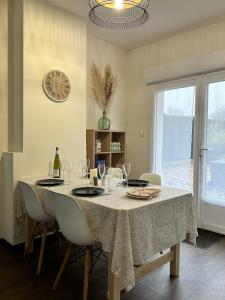 Le Gîte de la Maison Blanche في FlÃ©chin: غرفة طعام مع طاولة مع كؤوس للنبيذ وساعة