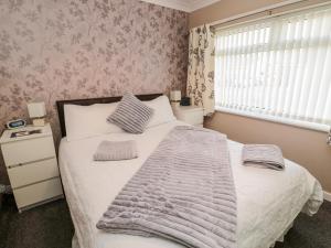 a bedroom with a white bed with a blanket and a window at Megstone in Beadnell