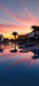 una piscina con palmeras y una puesta de sol en el fondo en Apartments Las Brisas Costa Adeje en Adeje