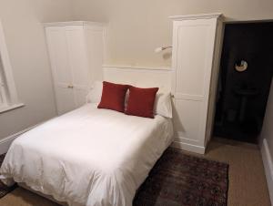 a white bed with two red pillows on it at La Montagne Observatory in Cape Town
