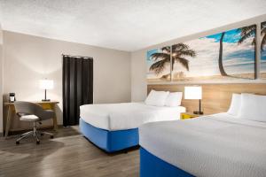 a hotel room with two beds and a desk and a chair at Days Inn by Wyndham Miami Airport North in Miami