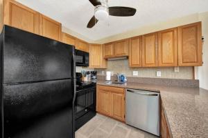 a kitchen with a black refrigerator and wooden cabinets at Kauai Banyan Harbor B24 condo in Lihue
