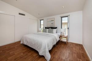 a white bedroom with a large bed and wooden floors at Groves Sunset Views in Aspendale in Aspendale