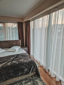 a bedroom with large windows with white curtains and a bed at Private Chalet in Moieciu de Jos