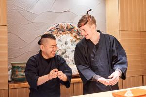 Dwóch mężczyzn stojących w kuchni i patrzących na coś. w obiekcie 泊まる寿司屋一力 Sushi house w mieście Itoshima