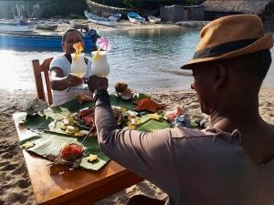 dos personas sentadas en una mesa con comida en la playa en ECOHOTEL LILI, en Puerto Limón