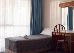 a bedroom with a bed with a desk and a chair at Holiday Lodge Motor Inn in Narooma