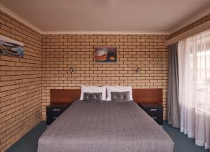 a bedroom with a bed and a brick wall at Coastal Comfort Motel in Narooma