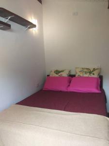 Bett in einem Zimmer mit rosa Bettwäsche und Kissen in der Unterkunft Chalé Praia de Boiçucanga in Boicucanga