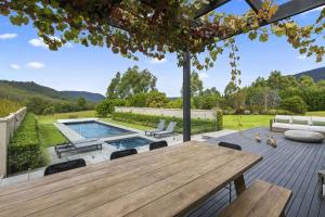 a patio with a wooden table and chairs and a swimming pool at Serendipity, Kangaroo Valley in Barrengarry